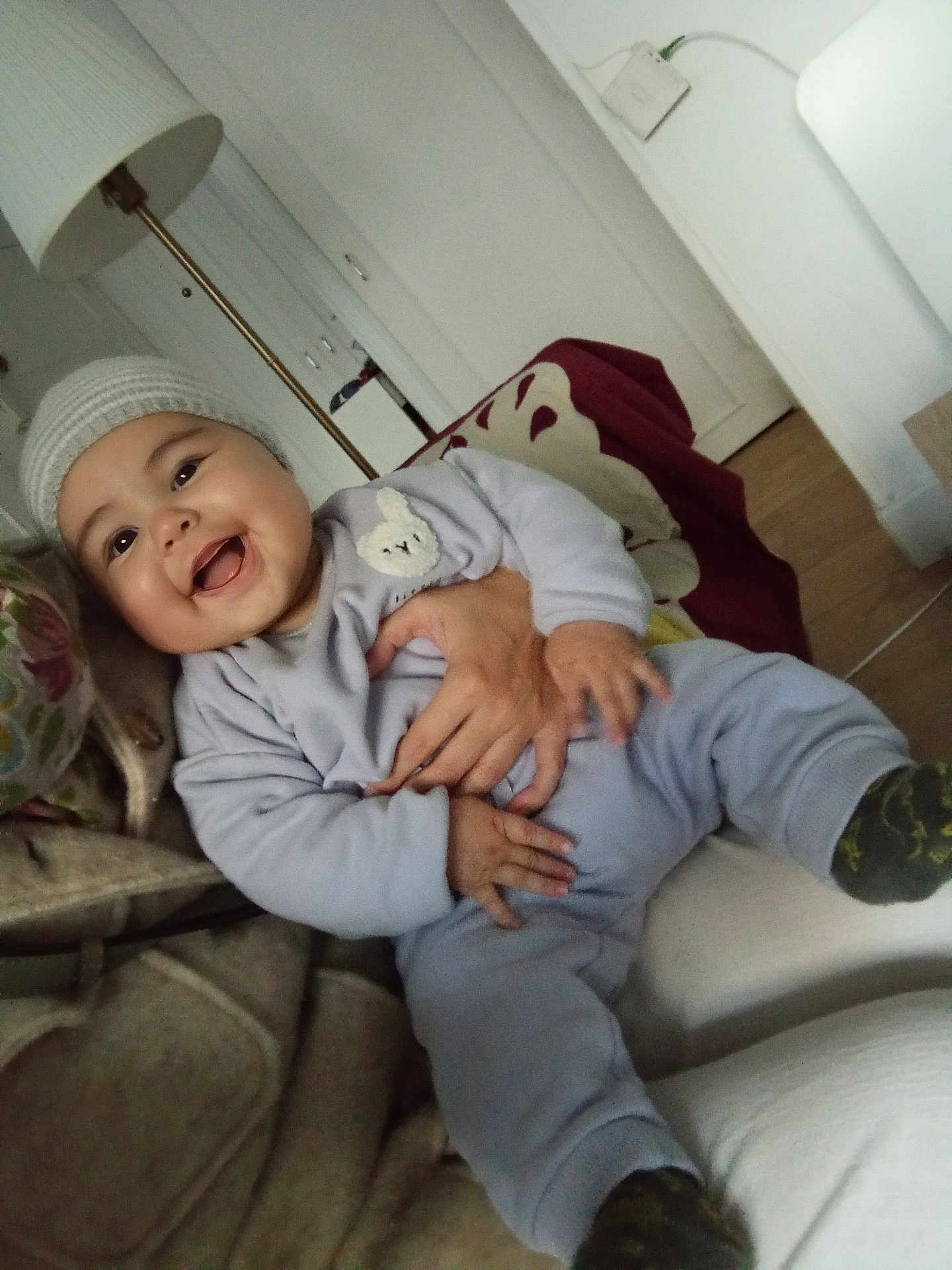 Helia a rejoint le concours — aidez-le/la à gagner de superbes lots ! baby, child, smiling, happy, indoor, hat, clothing, person, couch, blanket, hand, lamp, face, infant, warm, cozy, sitting, home, cute, portrait