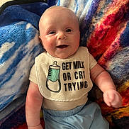 Jaiden is registered to the contest to win money with this photo: baby, infant, smiling, bib, clothing, blanket, colorful, happy, cute, face, portrait, lying_down, blue_pants, soft_texture, child, young, skin, person, indoors, casual