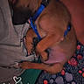animal, arms, bedtime, blanket, blue_harness, close_up, cozy, cuddle, curled_up, dim_lighting, dog, indoors, person, pet, portrait, puppy, relaxed, sleeping, snuggling, text