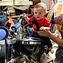 Scott joined the competition — help win amazing prizes! baby, child, person, motorbike, dirt_bike, red_shirt, spider_man, indoor, cluttered_background, hand_support, smiling, seat, foot, toy, garage, helmet, grip, handlebar, engine, stool