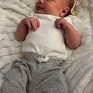 Waylon is registered to the contest to win money with this photo: baby, newborn, infant, sleeping, pacifier, onesie, blanket, soft_texture, gray_pants, sock, hands, face, head, portrait, cozy, peaceful, indoor, lying_down, closeup, adorable