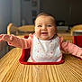 baby, child, high_chair, bib, smile, happy, table, wood, indoor, person, infant, cute, pink_clothing, long_sleeve, face, cheeks, expression, sitting, arm, room