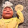 baby, baby_clothing, child, closeup, cute, flower, fluffy_rug, headband, indoor, infant, lying_down, milestone, newborn, one_month, person, portrait, smile, soft_texture, wooden_sign, yellow_onesie
