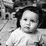 child, toddler, portrait, black_and_white, curly_hair, big_eyes, white_shirt, indoor, decor, blurred_background, cute, face, expression, young_child, looking_up, close_up, soft_light, baby, playful, monochrome