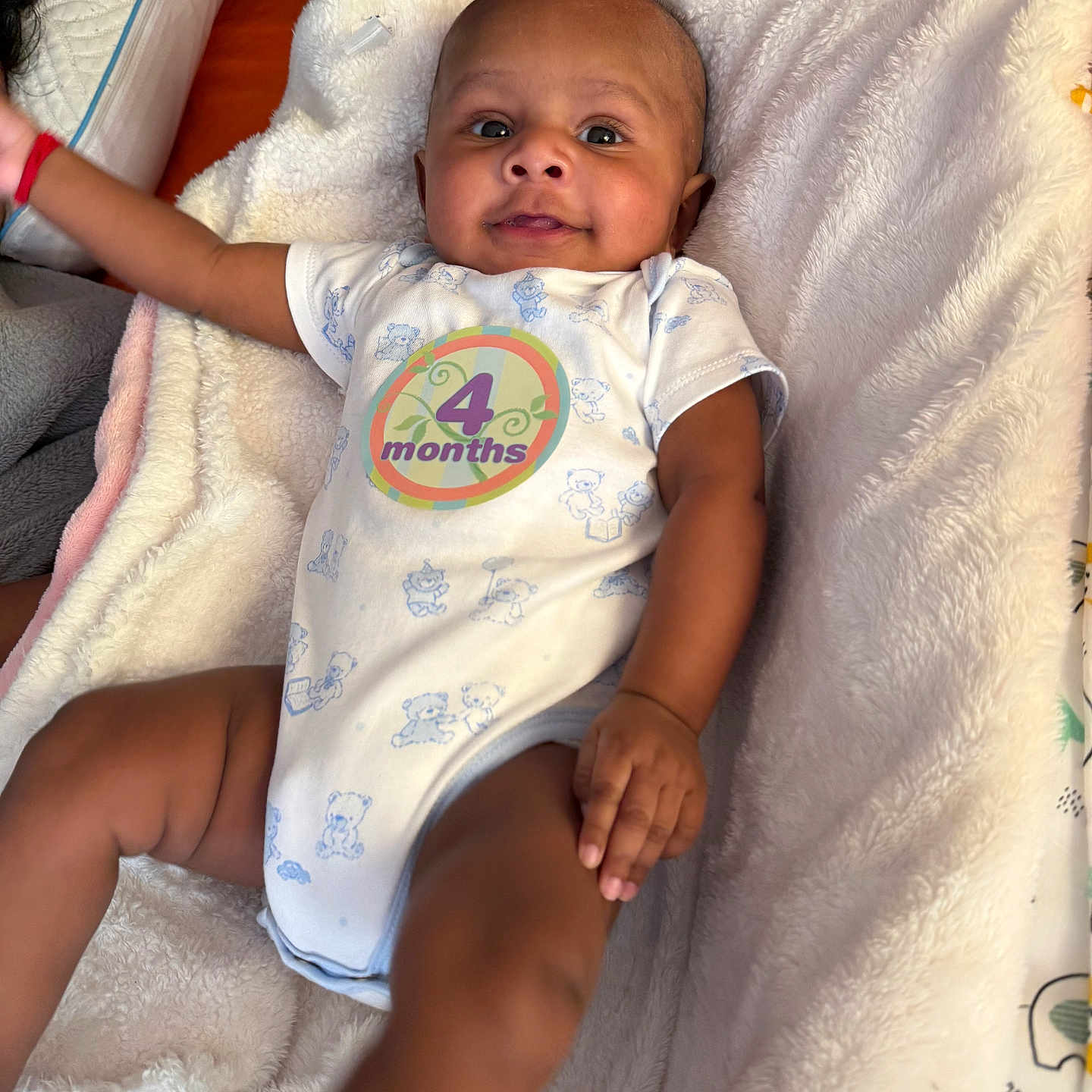 Kiran is registered to the contest to win money with this photo: arm, baby, blanket, child, comfort, cute, fabric, hand, happy, head, indoors, infant, leg, lying_down, onesie, portrait, skin, smiling, soft, sticker
