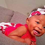 Summer is registered to the contest to win money with this photo: baby, child, smiling, drooling, headband, red_clothing, ladybug_pattern, couch, gray_couch, indoor, portrait, happy, cute, infant, young_child, person, skin, face, earrings, lying_down