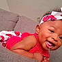 baby, child, smiling, drooling, headband, red_clothing, ladybug_pattern, couch, gray_couch, indoor, portrait, happy, cute, infant, young_child, person, skin, face, earrings, lying_down