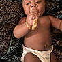 baby, diaper, bracelet, snack, lying_down, person, skin, hand, face, mouth, food, blanket, pattern, comfort, infant, cute, indoors, young_child, resting, casual
