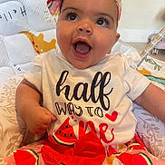 Wynter is registered to the contest to win money with this photo: baby, child, smiling, happy, headband, watermelon, dress, flower, patterned_clothing, cushion, indoor, portrait, cute, infant, sitting, bright_colors, face, expression, toddler, playful