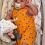 baby, pacifier, orange_outfit, polka_dots, plush_toy, blanket, soft_fabric, infant, cute, child, lying_down, clothing, comfort, indoors, hand, foot, face, portrait, sleeping_area, toddler