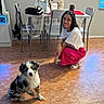 Pluto is registered to the contest to win money with this photo: woman, dog, puppy, indoor, floor, tile, table, chair, flowers, bag, smile, curly_hair, glasses, casual_clothing, white_shirt, pink_skirt, pet, home, window, mug