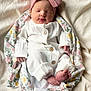 baby, newborn, infant, sleeping, white_clothing, headband, pink_bow, blanket, floral_pattern, soft_texture, wooden_buttons, cozy, cute, peaceful, portrait, indoors, closeup, small_feet, hands, resting