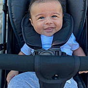Nassim Djellouah a rejoint le concours — aidez-le/la à gagner de superbes lots ! baby, child, stroller, smile, happy, infant, seatbelt, clothing, white_shirt, gray_pants, cute, portrait, outdoor, person, young_child, cheeky_smile, closeup, baby_face, safety_harness, casual_wear