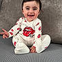 Natalia joined the competition — help win amazing prizes! baby, child, smiling, onesie, white_clothing, red_logo, rolling_stones_logo, sitting, peace_sign, happy, indoor, couch, gray_background, cute, portrait, infant, expression, face, person, footed_pajamas