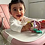 baby, child, smiling, high_chair, toy, teething_ring, pink, white_clothing, indoor, happy, cute, portrait, infant, hand, face, person, kitchen, seat, bright, playful