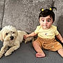 baby, child, dog, puppy, couch, sofa, pet, indoor, person, sitting, yellow_shirt, brown_skirt, cute, small_dog, fur, face, hair, barefoot, expression, home