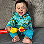 baby, child, smiling, happy, toy, pigtails, hoodie, colorful_clothing, sitting, barefoot, indoor, couch, gray_background, playful, infant, cute, expression, portrait, human, young