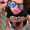 Deidara joined the competition — help win amazing prizes! baby, child, glasses, hand, tattoo, smile, tongue_out, person, indoor, flooring, black_clothing, adult, holding, funny_face, playful, closeup, portrait, expression, human, casual