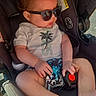 baby, child, infant, sunglasses, car_seat, seated, outdoor, sunlight, portrait, face, blonde_hair, white_shirt, shorts, palm_tree_pattern, fashion, relaxed, 安全, vehicle, harness, family_photo