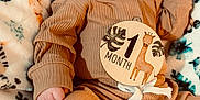 Lincoln joined the competition — help win amazing prizes! baby, infant, one_month, milestone, wooden_badge, giraffe, brown_clothing, ribbed_fabric, hat, blanket, lion_pattern, leaf_pattern, plush, cute, portrait, lying_down, indoors, child, person, newborn