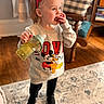 child, toddler, girl, red_bow, sippy_cup, snack, indoor, living_room, carpet, sweatshirt, mickey_mouse, pluto, black_pants, black_shoes, wood_floor, furniture, couch, cute, portrait, standing