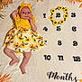 Paisley joined the competition — help win amazing prizes! baby, infant, yellow_headband, yellow_dress, sunflower_pattern, blanket, numbers, months, flower_ring, lying_down, cute, smiling, indoor, soft_texture, child, portrait, baby_clothes, headwear, skin, feet