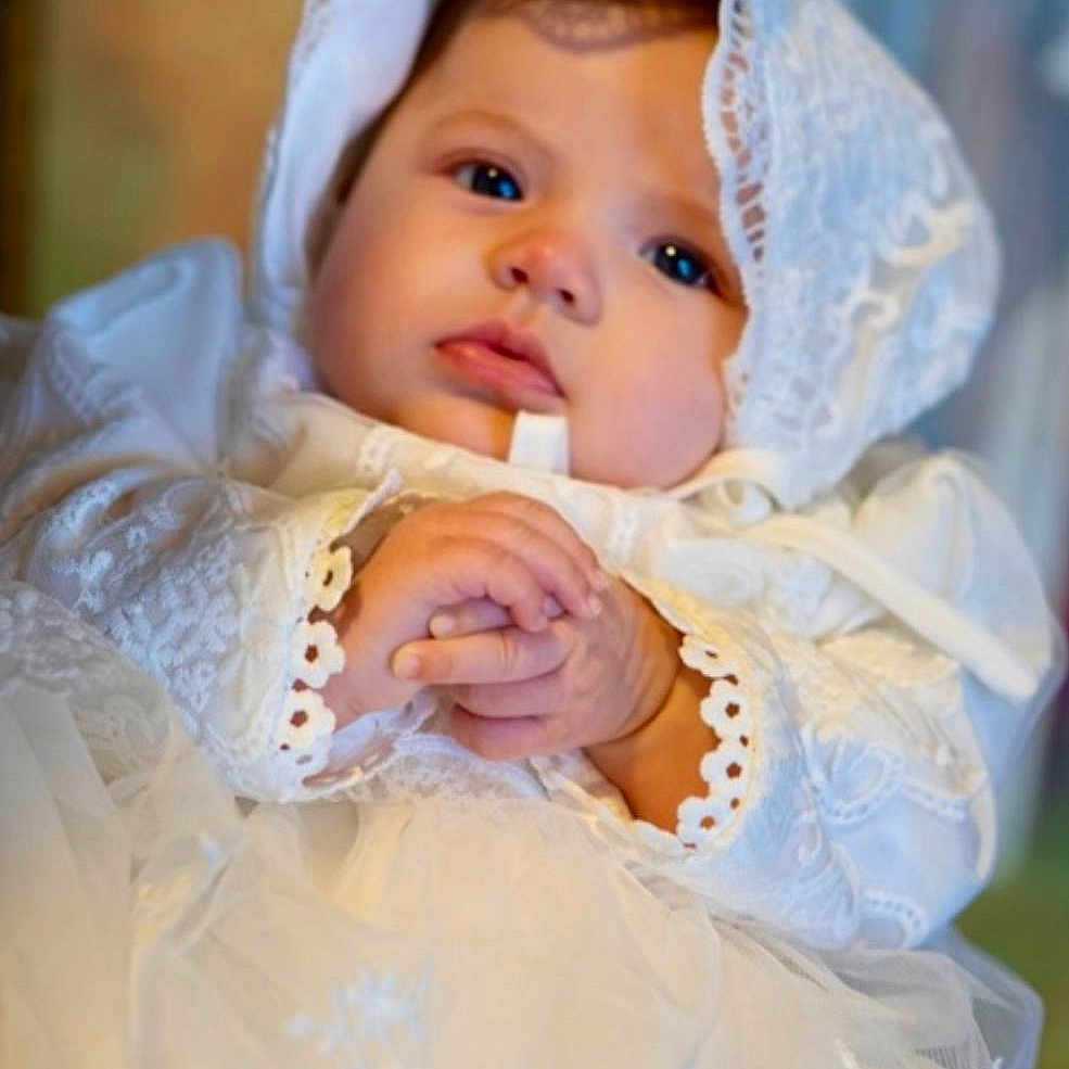 Scarlett Hopkins is registered to the contest to win money with this photo: baby, infant, lace, white_dress, bonnet, hands, clasped_hands, portrait, closeup, soft_lighting, cute, child, face, young, indoors, serene, adorable, clothing, expression, newborn