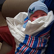 David is registered to the contest to win money with this photo: newborn, baby, infant, blanket, blue_hat, airplane_patch, hospital_blanket, wrapped, sleepy, cradled, couch, leather, person, indoors, cozy, child, cute, small, resting, baby_clothing