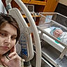 David is registered to the contest to win money with this photo: woman, newborn, hospital_bed, baby, hospital_room, medical_equipment, bassinet, wooden_cabinet, blanket, sleeping, patient, hospital_gown, indoor, mother, person, resting, face, hand, bedside, newborn_hat