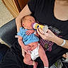David joined the competition — help win amazing prizes! newborn, baby, bottle, feeding, infant, diaper, blue_shirt, adult, arm, hospital_wristband, indoor, chair, wooden_cabinet, person, clothing, hand, skin, face, care, parent