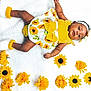 baby, infant, child, sunflower, yellow, white_blanket, flowers, headband, cute, smiling, lying_down, soft_texture, baby_clothes, footwear, bright_colors, portrait, indoors, happy, skin, baby_girl