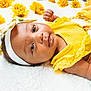 baby, infant, yellow_clothing, headband, flowers, blanket, lying_down, cute, child, portrait, close_up, soft_texture, floral_pattern, pacifier, skin, face, eyes, hand, adorable, bright_colors