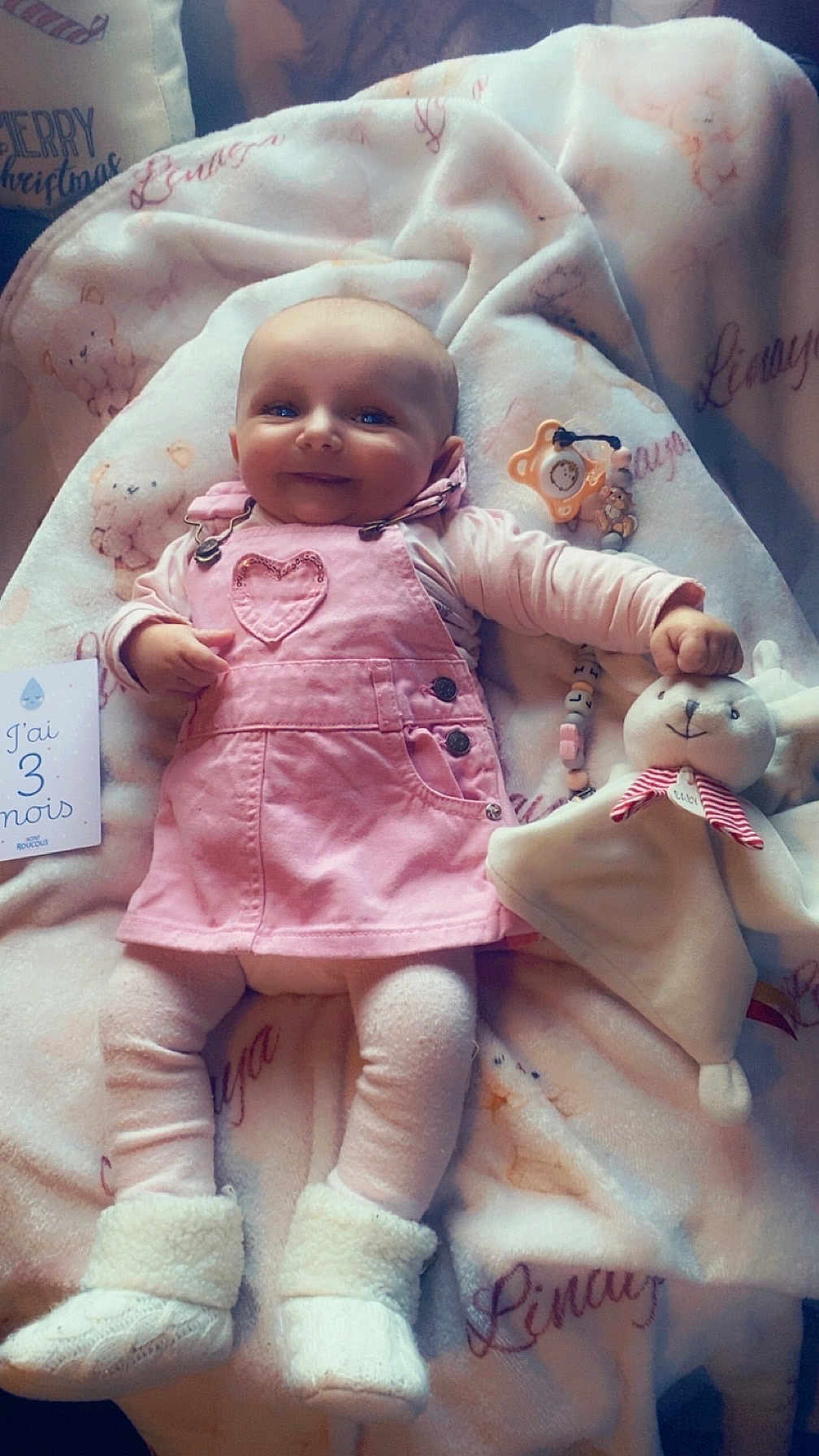 Linaya a rejoint le concours — aidez-le/la à gagner de superbes lots ! baby, bedding, blanket, booties, cozy, happy, infant, legs, lying_down, overalls, pacifier_clip, pinafore, pink_clothes, plush, portrait, smile, soft_texture, stuffed_animal, three_months, toy