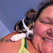 Gizmo is registered to the contest to win money with this photo: person, smile, puppy, dog, close_up, cuddle, freckles, curly_hair, tattoo, shoulder, green_top, indoor, face, pet, happy, resting, cute, companion, animal, skin