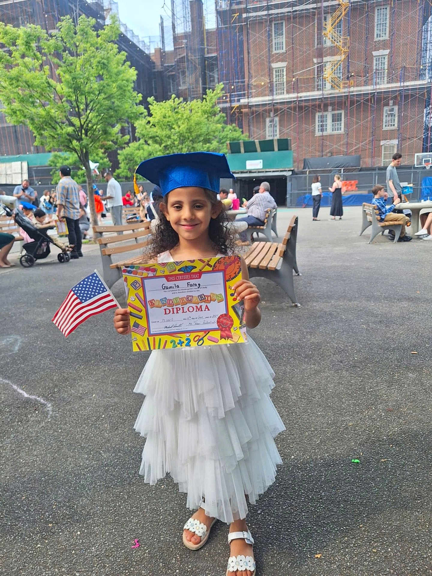 Gamila Farag joined the competition — help win amazing prizes! child, girl, graduation, diploma, cap, flag, white_dress, outdoor, celebration, people, bench, smile, curly_hair, sandals, pavement, urban, daytime, park, happy, event