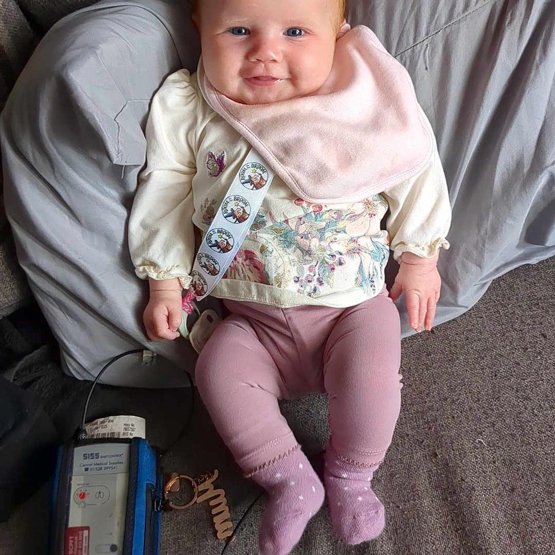 Dolly-Mae joined the competition — help win amazing prizes! baby, bib, child, couch, cute, fabric, happy, home_interior, indoors, infant, keychain, medical_device, person, pillow, pink_clothing, portrait, relaxing, smiling, socks, soft_lighting