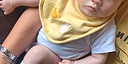 Dolly-Mae is registered to the contest to win money with this photo: adult_arm, baby, blue_eyes, bracelet, child, closeup, couch, curious, cute, diaper, indoor, infant, person, portrait, sitting, sock, watch, white_clothing, yellow_bib, yellow_shirt