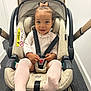 toddler, child, stroller, car_seat, harness, bow, pink_socks, indoor, carpet, smiling, pointing, baby_clothes, safety, seatbelt, cute, happy, person, infant, baby, transportation