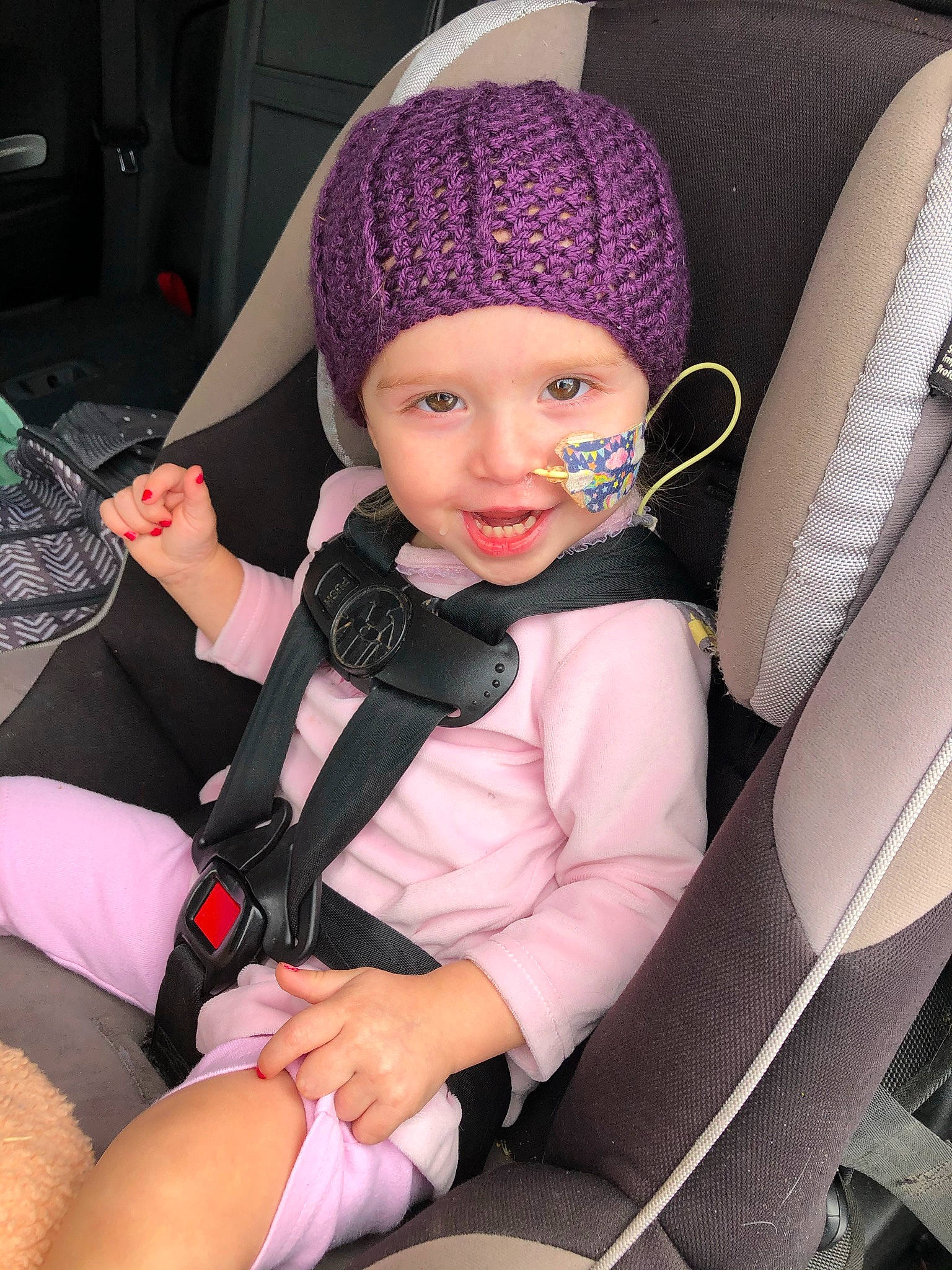 Aspen is registered to the contest to win money with this photo: automotive_design, baby_carriage, cap, car_seat, car_seat_cover, child, clothing, comfort, finger, hand, head_restraint, headwear, joy, lap, leg, person, pink, seat_belt, smile, steering_wheel
