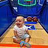 baby, child, basketball, basketball_hoop, court, sports, indoor, smiling, happy, floor, neon_light, blue_walls, sitting, toy, playful, footwear, shorts, tshirt, person, joyful