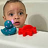 baby, bathtub, rubber_duck, toy_crab, child, bath_time, curious, wet_hair, face, water_drops, expression, indoor, playful, plastic_toy, bathroom, skin, head, large_eyes, pink_hearts, red