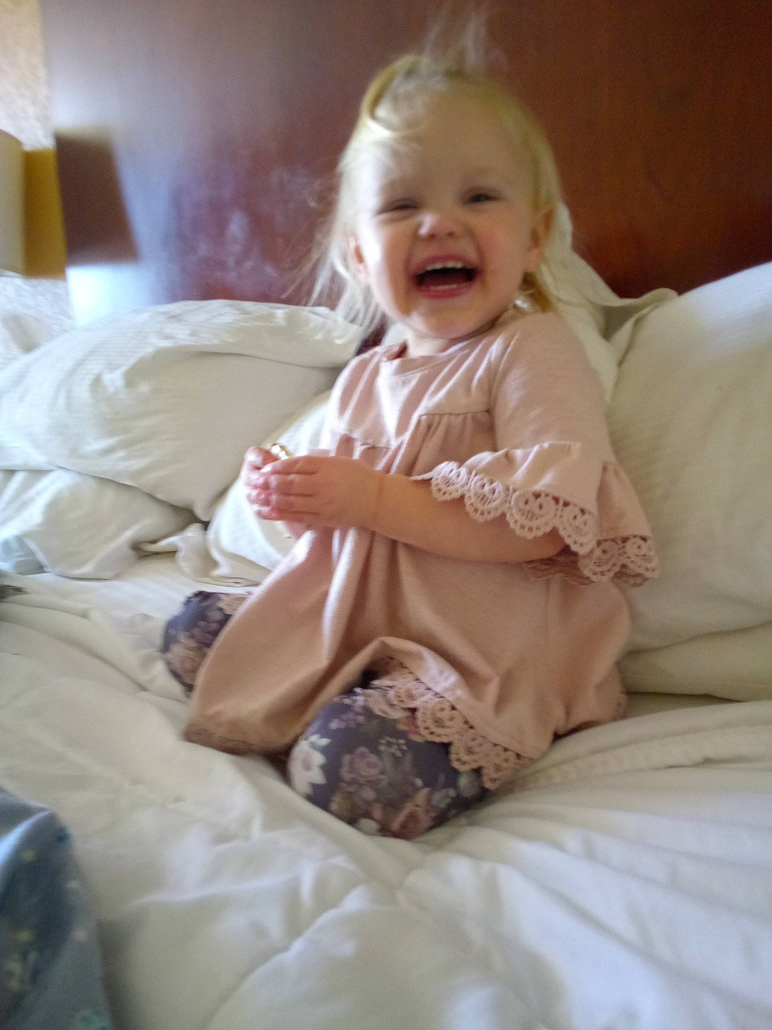 Zuri is registered to the contest to win money with this photo: baby, baby_toddler_clothing, bed, bedding, bedroom, child, comfort, dress, eye, flooring, fur, happy, head, human_body, linens, person, room, sitting, sleeve, smile