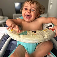Connor is registered to the contest to win money with this photo: toddler, baby_walker, smiling, happy, indoor, child, colorful, patterned, arms, legs, seat, furniture, person, skin, hair, playful, joyful, expression, excitement, home