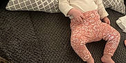 Tyana participe au concours pour gagner de l'argent avec cette photo : baby, infant, pillow, blanket, patterned_pillow, floral_pants, white_shirt, barefoot, indoors, lying_down, face, person, cute, cozy, soft_texture, curious, resting, home, child, comfort