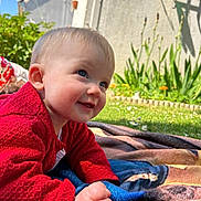 Esmée a rejoint le concours — aidez-le/la à gagner de superbes lots ! baby, child, smiling, red_sweater, blanket, outdoor, grass, flowers, garden, face, blue_eyes, skin, hand, crawling, daylight, sunny, person, head, happy, nature