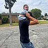 Noah joined the competition — help win amazing prizes! baby, child, man, shoulders, street, suburban, tree, house, cloudy_sky, jeans, black_shirt, cap, grass, sidewalk, outdoor, smiling, person, daytime, casual, holding