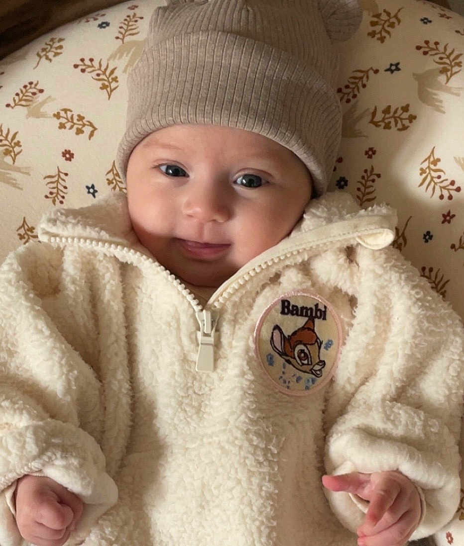 Lorena a rejoint le concours — aidez-le/la à gagner de superbes lots ! baby, infant, hat, knit_hat, jacket, fleece_jacket, bambi_patch, smile, face, hand, patterned_cushion, cute, child, portrait, warm_clothing, indoor, closeup, soft_texture, young_child, cozy