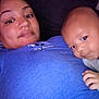 James is registered to the contest to win money with this photo: adult, baby, child, person, face, couch, pillow, dinosaur_pattern, blue_shirt, indoor, portrait, closeup, relaxing, snuggling, hand, looking, casual, resting, family, bonding