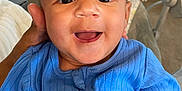 James is registered to the contest to win money with this photo: baby, child, blue_clothing, smiling, happy, face, hand, indoor, couch, toy, person, infant, cute, portrait, home, supporting_hand, sitting, young_child, cozy, zipper