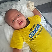 James is registered to the contest to win money with this photo: baby, infant, yellow_shirt, crib, blanket, mittens, smile, face, child, cute, lying_down, comfort, soft, indoors, toddler, happy, clothing, person, young_child, expression